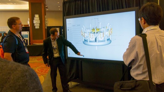 A workstation was scheduled to be driving the 82” Perceptive Pixel touchscreen, but a Microsoft Surface Pro filled in when the workstation died in transit. Microsoft’s Simon Floyd, center, shows attendees at the Siemens PLM Software users conference how to use the touch capabilities. (Source: Siemens PLM)