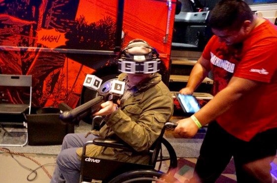 They’ll be prying that plastic rifle out of his cold dead fingers. Gamers get a chance to play the Walking Dead VR demo by Starbreeze Studios. Note man behind the player with the tablet is monitoring where the player is in the game – occasionally, he’ll shake the wheel chair so the player feels like the wheelchair is being pushed through a zombie-infested warehouse. (Source: JPR)